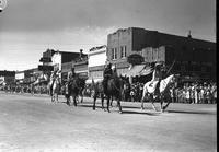 [Six Indian men on horseback in parade; buildings and spectators in background]