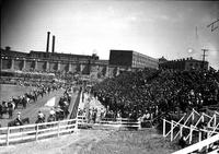 [Two lines of rodeo persons on horseback in arena with spectator-crowded stands to right]