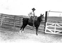 [Eddie McCarty in striped shirt and tie on horse in front of fence and gate]