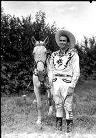 [Buff Brady Jr. in white suit with flower trim standing with white horse]