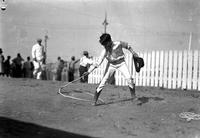 [Unidentified young cowboy spinning a rope loop around one foot]