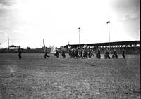 [Cowboy marching band members taking position on field with tipi in background]