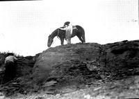 [Unidentified cowgirl with horse atop outcropping]