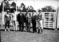 [Six men in line in front of cattle pens; Two in business attire, four in western wear]