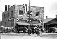 [Six horse team pulling carriage of passengers past "Jackson Drug Co."]