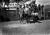 [Unidentified Cowboy & cowgirl on horseback side be side in front of chutes]