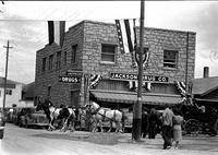 [Six horse team pulling carriage of passengers past "Jackson Drug Co."]