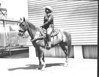 [Unidentified cowgirl on horse in front of building]