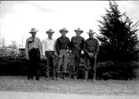 [Five unidentified cowboys standing in front of low shrubbery]