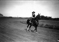 [Unidentified cowgirl on horseback galloping around racetrack]