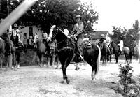 [Unidentified Cowgirl on horseback; others in background preparing for parade]