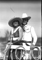 [Unidentified cowgirl and cowboy standing together closely near ropes]