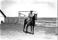 [Unidentified Cowboy with rope on saddle in front of corral]