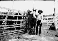 [Unidentified rodeo clown standing by corral of horses with mule and cowboy]