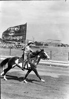 [Unidentified cowboy on galloping horse on track bearing a Swifts Jewel Flag]