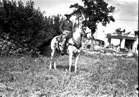 [Possibly Earl Strauss with rope in hand mounted on horse with trick riding saddle]