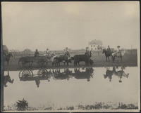 [6 cowgirls on horseback with a wagon drawn by oxen, white house in background, reflection in water]