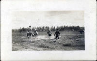 Unidentified saddle bronc rider on ground as clown and others look on