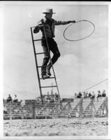 Unidentified cowboy on a ladder balancing on a tight rope while spinning rope