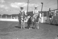 [Unidentified cowgirl, little girl, and cowboy posed on horses near chutes]