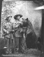 [Two hunters with stuffed bear and rifle]