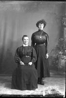 [Single portrait of two Females, aged sitting, young standing]