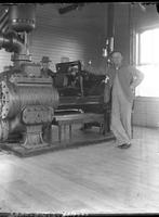 [Two men standing by machinery inside building in Shawnee]