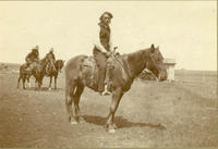 [Indian man posed atop horse with three other riders behind]
