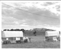[Covered wagons in foreground with distant view of museum]