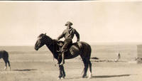 [Unidentified cowboy in profile atop saddled horse]