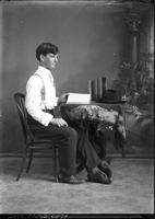 [Single portrait of a young Man at table with books]