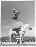 Unidentified cowboy spinning rope atop horse