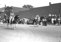 [Two unidentified cowboys on horses in street for parade]