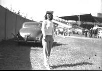 [Unidentified cowgirl posed in front of automobile]