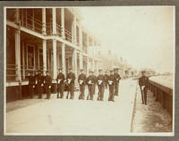 [Military men at attention with 3 buglers blowing all standing perhaps a boardwalk]