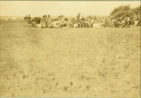 [Indian women and children sitting on ground in distance, tipis further in distance, social event]