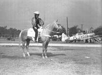 [Unidentified cowgirl posed on horse with  army plane behind]