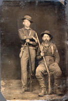 [Two men, one sitting one standing, both with rifles in studio poses]