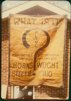 [Photograph of Advertising Banner: "What is It?"