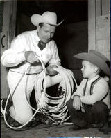 [A kneeling Junior Eskew explains details of trick roping to a sitting young boy]