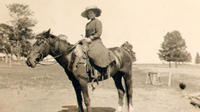 [Unidentified woman in hat & dress atop saddled horse]