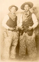 [Two posed standing "cowboys" wearing wooly chaps]