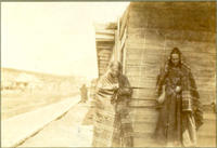 [Two Indian women standing with backs to dilapidated building]