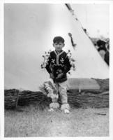 [Young Native American boy in Native dress standing in fron of tipi]