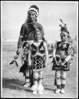 [Native American person and two Native American children, all in costume]