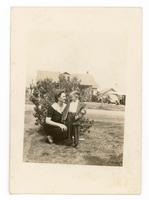 [Woman and little boy standing near a bush]