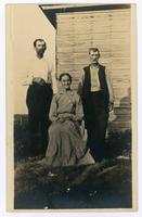 2 men and a woman (she is sitting in a chair) near a house]