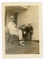 [2 men sitting in chairs on a front porch]