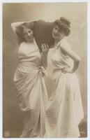 [Two women posed together in simple white gowns with heart prop] 779/4