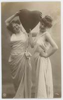 [Two women posed together in simple white gowns with heart prop] 779/3